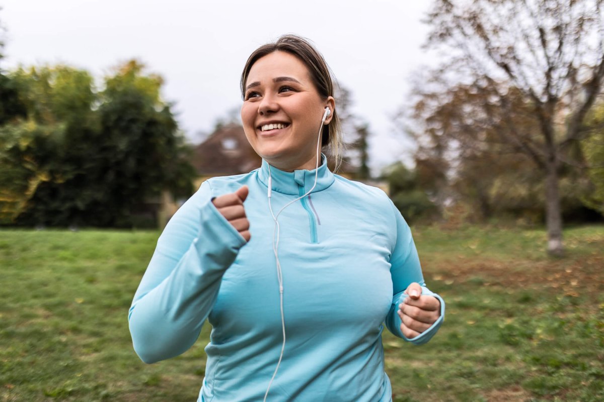 Smiling woman jogging in a light-blue athletic jacket.